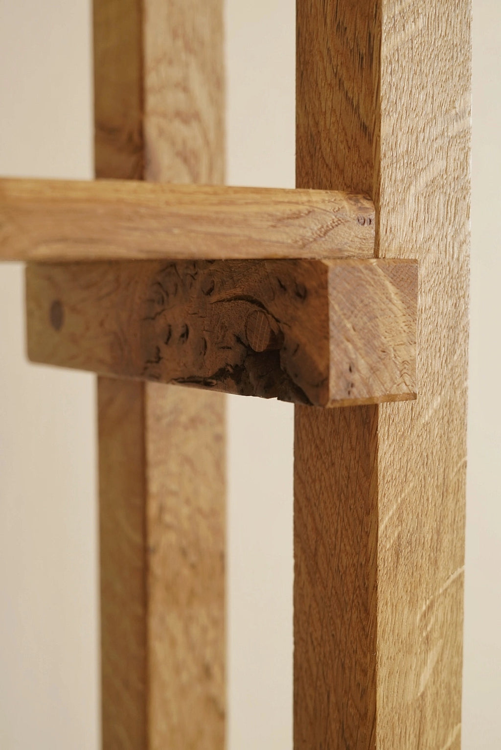Close-up of a rustic wooden furniture piece showing natural oak wood grain, a carved wooden support beam, and a light beige background.
