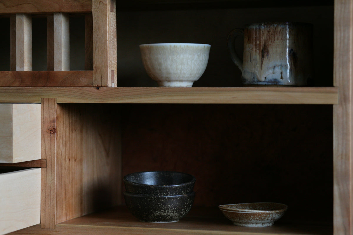 Close up of a cherry tea cabinet showcasing ceramic tea cups. 