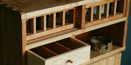Wooden tea cabinet with open drawer on a dark background.